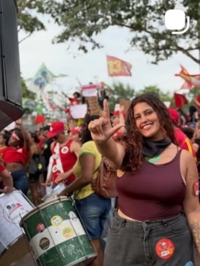 Jovem sorridente com tambor no meio de um ato com bandeiras